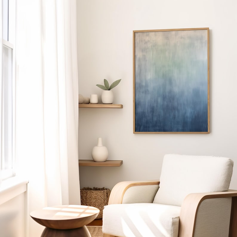 Pode incluir: Uma pintura abstrata emoldurada em madeira, apresentando um gradiente de cores do bege claro ao azul profundo. A obra de arte est&aacute; pendurada numa parede branca, complementada por uma poltrona branca, prateleiras de madeira e vasos decorativos. O quarto &eacute; luminoso.