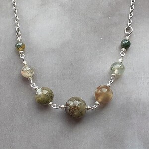 May include: A silver chain necklace with six round green, brown, and white gemstone beads.