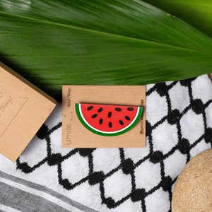 Può includere: Uno spillo in legno a forma di fetta di anguria con un centro rosso, semi neri e una buccia verde. Lo spillo è su una carta marrone con il testo "Umile Wood Things" e "@umilewoodthings".