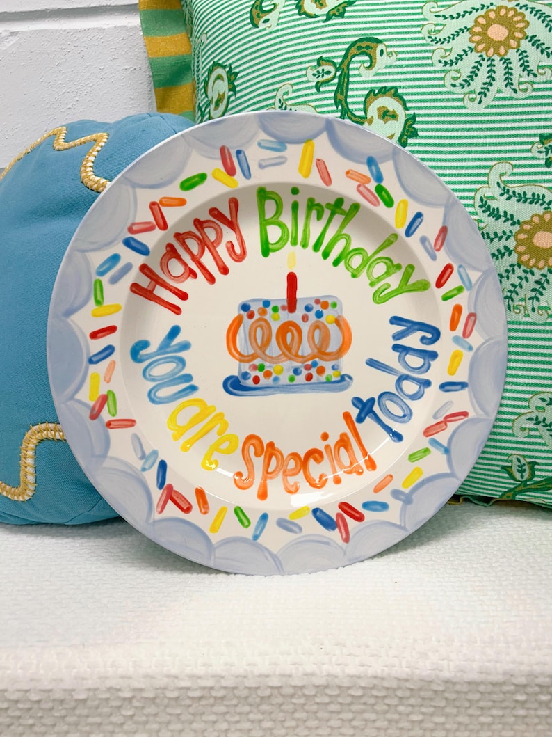 May include: A white ceramic plate with a blue scalloped edge and colorful text that reads "Happy Birthday Today You are Special!" A small cake with a lit candle is in the center, surrounded by colorful sprinkles.