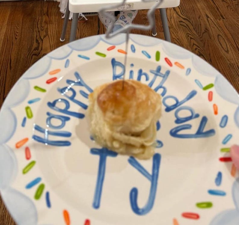 May include: A birthday cake on a decorative plate. The plate has a blue border and the words "Happy Birthday Ty" written in blue. The cake is topped with a star-shaped decoration.