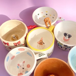 May include: A collection of ceramic mugs featuring different dog figurines inside. The mugs are decorated with various patterns, including polka dots, hearts, and flowers.