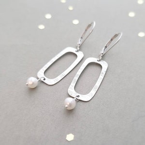 May include: Silver earrings with a rectangular shape and a small white pearl dangling from each earring.
