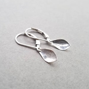 May include: A pair of silver earrings with a hammered, teardrop-shaped design. The earrings have a simple, minimalist style.