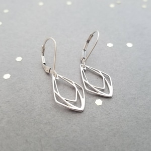 May include: A pair of silver dangle earrings with a geometric diamond shape design. The earrings have a leverback closure.