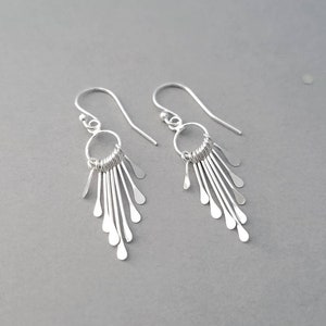 May include: Silver dangle earrings with a circle design and multiple thin strands hanging down.