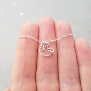 May include: A silver necklace with a delicate sloth pendant. The chain is thin and the sloth is hanging upside down.