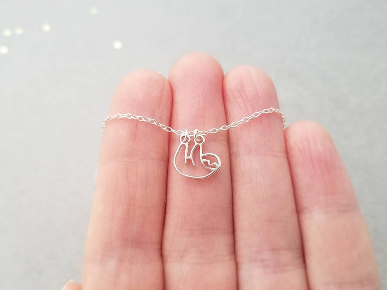 May include: A silver necklace with a delicate sloth pendant. The chain is thin and the sloth is hanging upside down.