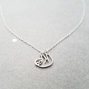 May include: A silver chain necklace with a delicate silver sloth pendant. The sloth is hanging upside down.