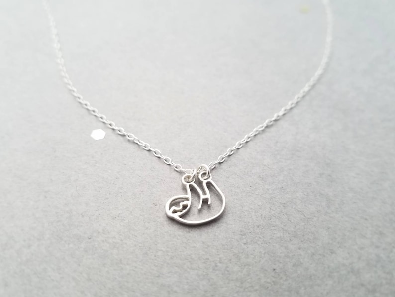 May include: A silver chain necklace with a delicate silver sloth pendant. The sloth is hanging upside down.