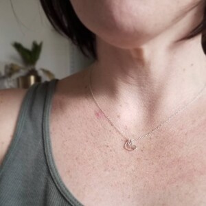 May include: A silver chain necklace with a small, delicate pendant featuring three interlocking circles. The necklace is worn by a person with a light complexion and short, dark hair.