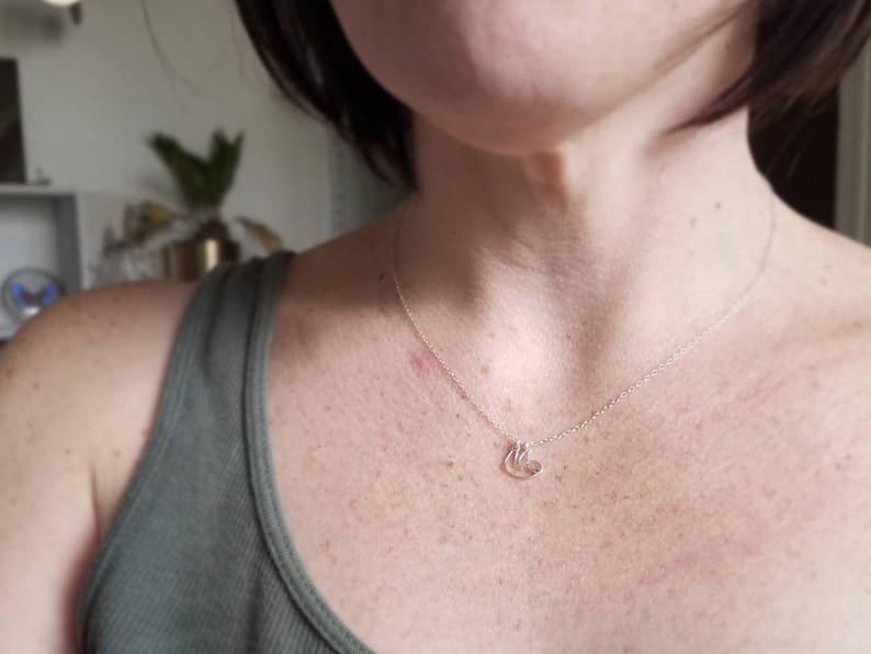 May include: A silver chain necklace with a small, delicate pendant featuring three interlocking circles. The necklace is worn by a person with a light complexion and short, dark hair.
