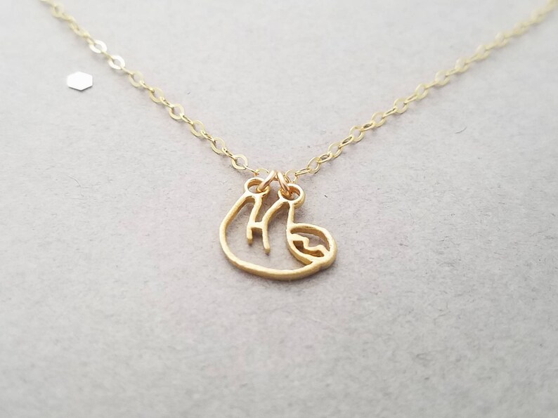 May include: A gold necklace with a delicate, cutout sloth charm. The chain is thin and delicate, and the sloth is hanging from a small loop.
