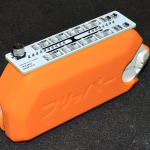 K&ouml;nnte beinhalten: Ein orangefarbenes elektronisches Ger&auml;t mit einer wei&szlig;en Leiterplatte oben. Die Leiterplatte hat mehrere kleine Lichter und den Text "Infrared Dazzler". Das Ger&auml;t hat japanischen Text auf der Seite.