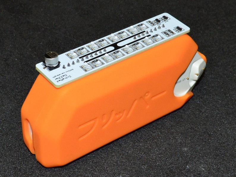 K&ouml;nnte beinhalten: Ein orangefarbenes elektronisches Ger&auml;t mit einer wei&szlig;en Leiterplatte oben. Die Leiterplatte hat mehrere kleine Lichter und den Text "Infrared Dazzler". Das Ger&auml;t hat japanischen Text auf der Seite.