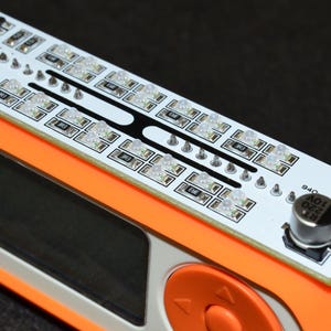 K&ouml;nnte beinhalten: Ein orangefarbenes elektronisches Ger&auml;t mit einer wei&szlig;en Leiterplatte mit mehreren LED-Leuchten. Die Platine ist mit "InfraRed Dazzler" beschriftet und hat einen kleinen Knopf. Das Ger&auml;t hat einen schwarzen Bildschirm und einen orangefarbenen Bedienknopf.