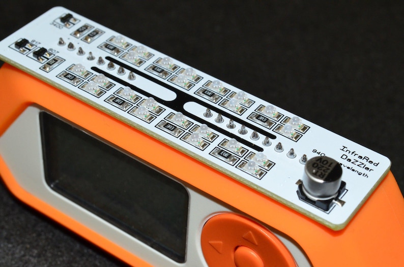 K&ouml;nnte beinhalten: Ein orangefarbenes elektronisches Ger&auml;t mit einer wei&szlig;en Leiterplatte mit mehreren LED-Leuchten. Die Platine ist mit "InfraRed Dazzler" beschriftet und hat einen kleinen Knopf. Das Ger&auml;t hat einen schwarzen Bildschirm und einen orangefarbenen Bedienknopf.