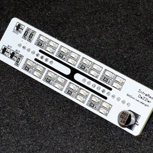 K&ouml;nnte beinhalten: Eine wei&szlig;e Leiterplatte mit zahlreichen kleinen rechteckigen Lichtern und dem Text "InfraRed DeZzIer 940nm wavelength". Die Platine hat verschiedene kleine Komponenten und ein kreisf&ouml;rmiges Element.