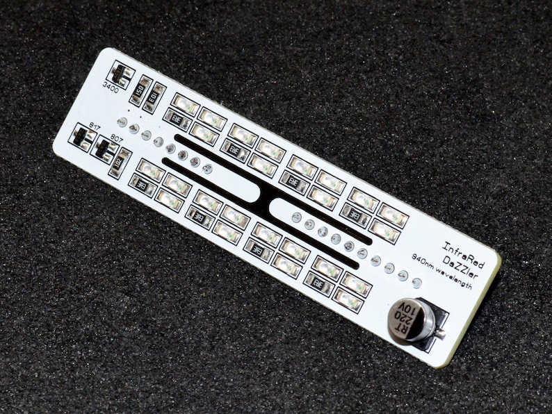 K&ouml;nnte beinhalten: Eine wei&szlig;e Leiterplatte mit zahlreichen kleinen rechteckigen Lichtern und dem Text "InfraRed DeZzIer 940nm wavelength". Die Platine hat verschiedene kleine Komponenten und ein kreisf&ouml;rmiges Element.