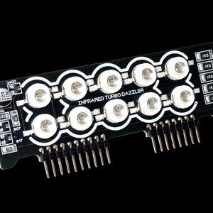 Może przedstawiać: Czarna płytka drukowana z napisem "INFRARED TURBO DAZZLER" i wieloma białymi diodami LED. Płytka posiada kilka pin&oacute;w i małe elementy elektroniczne. Tło jest jednolicie czarne.