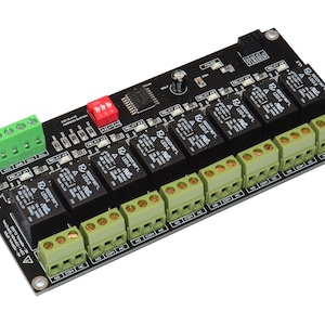 Peut inclure: Circuit imprimé noir avec plusieurs relais, des borniers verts et noirs et un commutateur DIP rouge. La carte comporte divers composants électroniques et étiquettes, pour projets électriques.