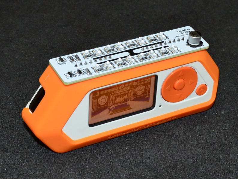 K&ouml;nnte beinhalten: Ein orange-wei&szlig;es elektronisches Ger&auml;t mit einem Bildschirm, der eine Grafik anzeigt. Es hat eine Leiterplatte oben mit LED-Leuchten und dem Text "Intrafied Gezza". Das Ger&auml;t hat ein orangefarbenes Bedienfeld mit einer kreisf&ouml;rmigen Taste.