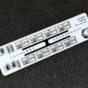 K&ouml;nnte beinhalten: Eine wei&szlig;e Leiterplatte mit der Aufschrift "InfraRed DaZZler" und dem Text "940nm wavelength". Sie verf&uuml;gt &uuml;ber zahlreiche kleine, rechteckige Lichter und ein schwarzes Designelement. Eine kleine Metallkomponente ist ebenfalls vorhanden. Auf dunklem Untergrund.