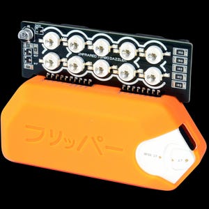 May include: An orange electronic device with the Japanese word "Flipper" printed on it, topped with a black circuit board. The circuit board has multiple white lights and the text "Infrared Turbo Dazzler".