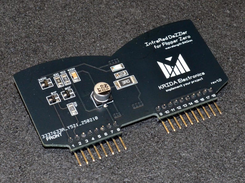 Puede incluir: Placa de circuito negra con pines dorados y componentes electr&oacute;nicos, etiquetada como "InfraRed DaZZier for Flipper Zero". La placa tiene el texto "KRIDA Electronics" y "rev1.0".