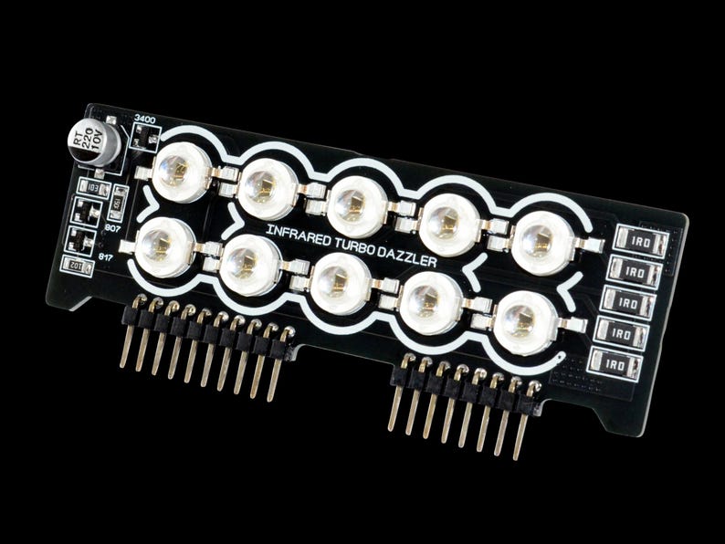Może przedstawiać: Czarna płytka drukowana z napisem "INFRARED TURBO DAZZLER" i wieloma diodami LED. Płytka posiada piny do podłączenia do innych urządzeń oraz kilka małych element&oacute;w elektronicznych.