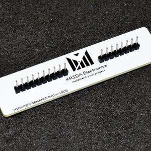 K&ouml;nnte beinhalten: Eine wei&szlig;e, rechteckige Leiterplatte mit schwarzen Steckern und silbernen Stiften. Die Platine tr&auml;gt den Text "KRIDA Electronics" und "Implement your project". Der Text "HIGH PERFORMANCE 940nm LEDs" ist ebenfalls sichtbar.