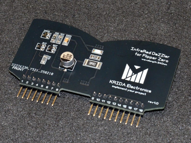 Puede incluir: Placa de circuito electr&oacute;nico negra con pines dorados, etiquetada como "InfraRed DaZZler for Flipper Zero". Cuenta con varios componentes y el texto "KRIDA Electronics" y "rev1.0".
