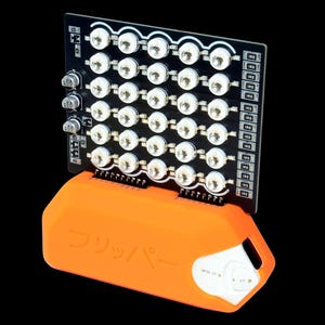 May include: A black circuit board with 48 white LED lights is mounted on an orange base. The base has Japanese text and a white control panel. The background is black.