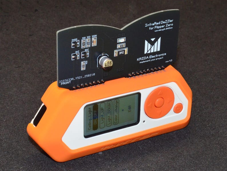 Puede incluir: Un dispositivo electr&oacute;nico naranja y blanco con una placa de circuito negro adjunta. La placa de circuito tiene varios componentes y el texto "InfraRed DaZZler for Flipper Zero". El dispositivo tiene una pantalla que muestra opciones y un bot&oacute;n de control naranja.