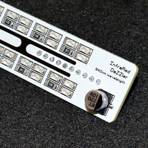 K&ouml;nnte beinhalten: Eine wei&szlig;e Leiterplatte mit mehreren kleinen, rechteckigen LED-Leuchten, die in Reihen angeordnet sind. Die Platine hat schwarze Akzente und den Text "InfraRed DaZZler 940nm wavelength". Ein kleines, silbernes Bauteil ist an der Platine befestigt.