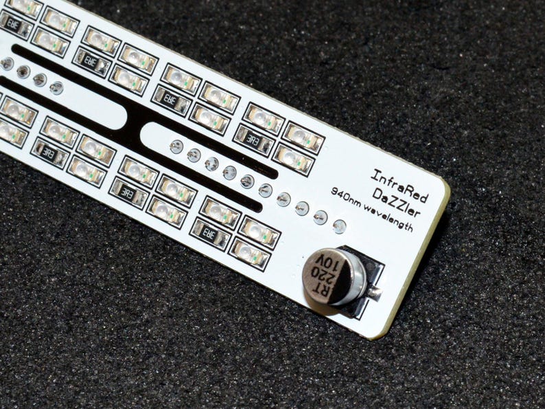 K&ouml;nnte beinhalten: Eine wei&szlig;e Leiterplatte mit mehreren kleinen, rechteckigen LED-Leuchten, die in Reihen angeordnet sind. Die Platine hat schwarze Akzente und den Text "InfraRed DaZZler 940nm wavelength". Ein kleines, silbernes Bauteil ist an der Platine befestigt.