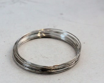 May include: A close-up of a silver wire wrapped into a circle, forming a ring. The wire is thin and shiny, and the ring is about 2 inches in diameter.