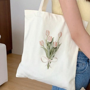 May include: A white canvas tote bag with a pink and green floral design featuring a bouquet of tulips tied with a pink ribbon.