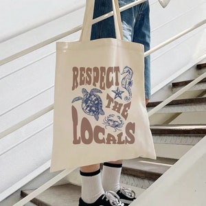 May include: A beige canvas tote bag with the text "Respect the Locals" in brown letters. The bag features a blue seahorse, a blue starfish, a blue sea turtle, and a blue crab.