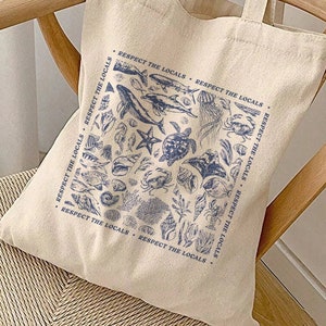 May include: A beige canvas tote bag with blue and white illustrations of sea life and the text "Respect the Locals" repeated around the bag.