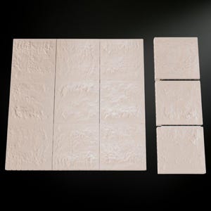 May include: A collection of beige, textured tiles arranged on a black surface. The tiles are square and have a rough, stone-like appearance. The arrangement includes a larger rectangular group and a smaller group of individual tiles.