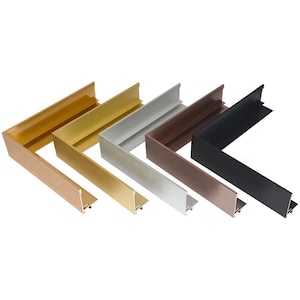 May include: A collection of L-shaped picture frame corners in various metallic finishes. The colors include light wood, gold, silver, bronze, and black. The frames are designed to be joined to create a complete picture frame.