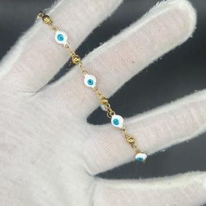 May include: A gold chain bracelet with white and blue evil eye charms.