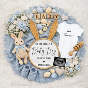 May include: A baby announcement with a light blue theme. The image includes a stuffed bunny, baby shoes, a onesie, and a wooden sign that reads "Baby Boy is on the way! October 2026." Decorative elements include flowers, eggs, and a baby rattle.
