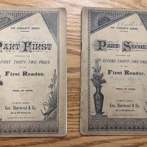 May include: Two antique First Reader books. The covers are tan with black text and illustrations. The first book is labeled "Part First" and the second "Part Second". Both books feature floral vase illustrations and text that reads "The Student's Series."