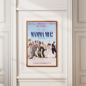 Op de afbeelding: Een ingelijste filmposter voor "Mamma Mia!" met een bruine lijst. De poster toont een cast van personages in formele kleding en bevat de tekst "THE FEEL-GOOD CINEMA EVENT OF THE SUMMER!" en "IN CINEMAS EVERYWHERE JULY 10".