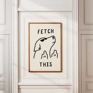 Könnte beinhalten: Gerahmter Kunstdruck mit einer minimalistischen schwarzen Strichzeichnung eines Hundes mit Sonnenbrille und den Worten "FETCH THIS". Das Kunstwerk hat einen cremefarbenen Hintergrund und einen braunen Holzrahmen.