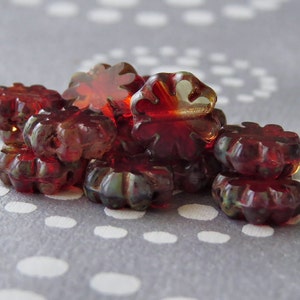 Puede incluir: Un grupo de cuentas de vidrio rojo con un diseño de estrella. Las cuentas son translúcidas y tienen un ligero brillo iridiscente.