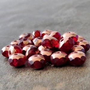 Puede incluir: Un montón de pequeñas cuentas de vidrio rojas facetadas con un acabado metálico de cobre.