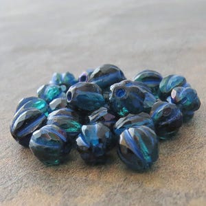 May include: A pile of dark blue glass beads with a ribbed texture. The beads have a slight iridescent sheen.
